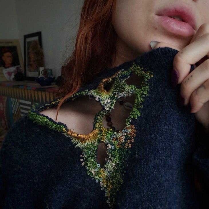 a woman with red hair wearing a blue sweater and holding her hand on her chest