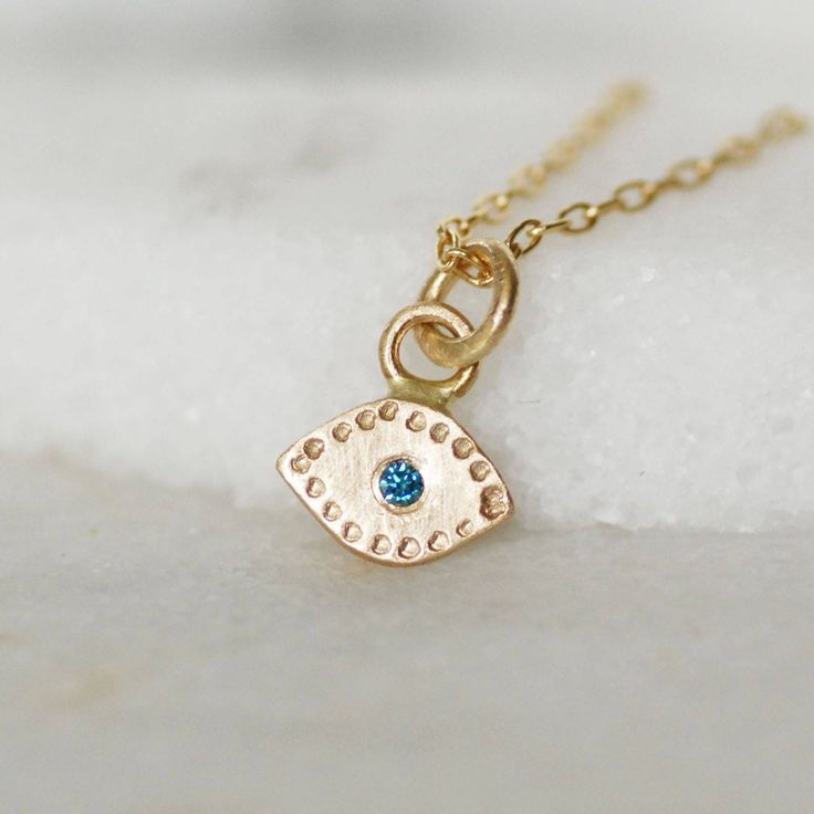 "Solid 14k Gold and teal blue Evil Eye modern minimalist charm necklace.  Handmade evil eye necklace set with a teal blue diamond center.  The charm hangs from a 1.3mm 14k yellow gold chain with  lobster clasp.  This dainty gold charm is the perfect size for everyday wear! Details: Eve dimensions - 8mm wide x 5mm tall (without bail) diamond - 1.7mm teal blue diamond (treated to enhance color) chain - 1.3mm cable chain with lobster clasp Length - Choose at checkout Made to order **Please note the photos are enlarged on your computer screen. Please refer to a ruler with the dimensions I have listed to ensure you are aware of the exact scale of the item before purchasing. Thank you! **Check out the rest of my necklace collection here: https://www.etsy.com/shop/LilianGinebra?ref=seller-platfor 14k Gold Evil Eye Jewelry Gift, Dainty 14k Gold Evil Eye Jewelry, Fine Jewelry With Blue May Birthstone, Fine Jewelry Blue May Birthstone, Blue Birthstone 14k Gold Jewelry, Blue Fine Jewelry For May Birthstone, Blue May Birthstone Fine Jewelry, Blue Round Pendant Jewelry For May Birthstone, Fine Jewelry 14k Gold Blue Birthstone Necklace