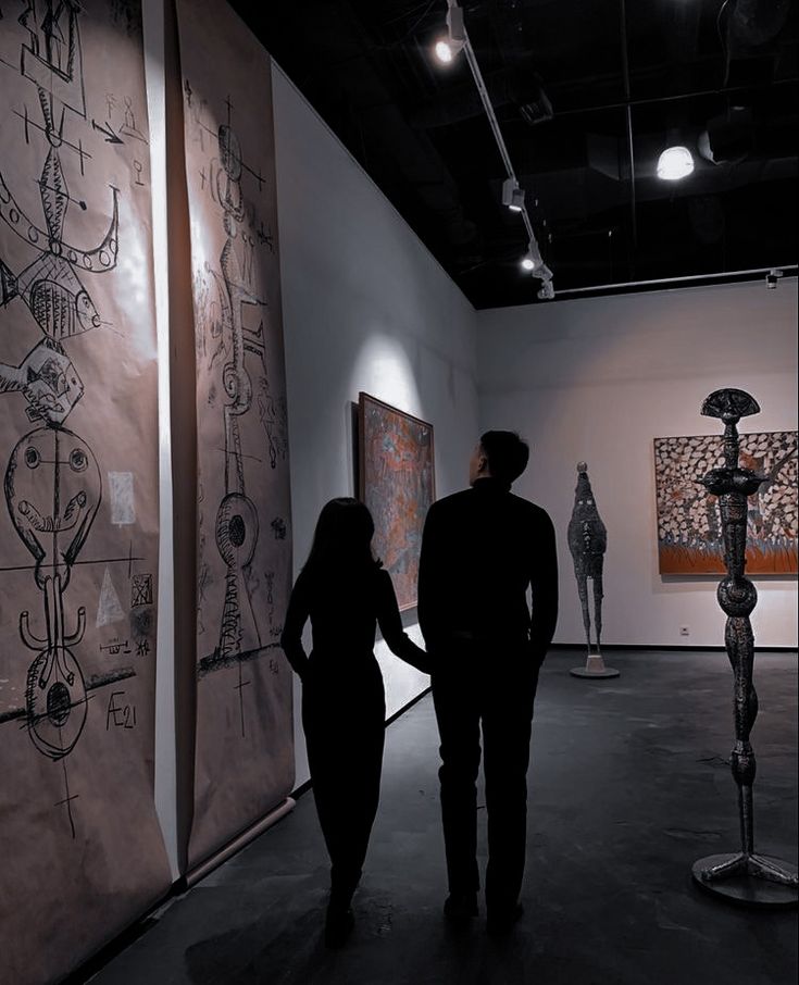 two people are looking at art on display in the dark, while one person is holding his hand