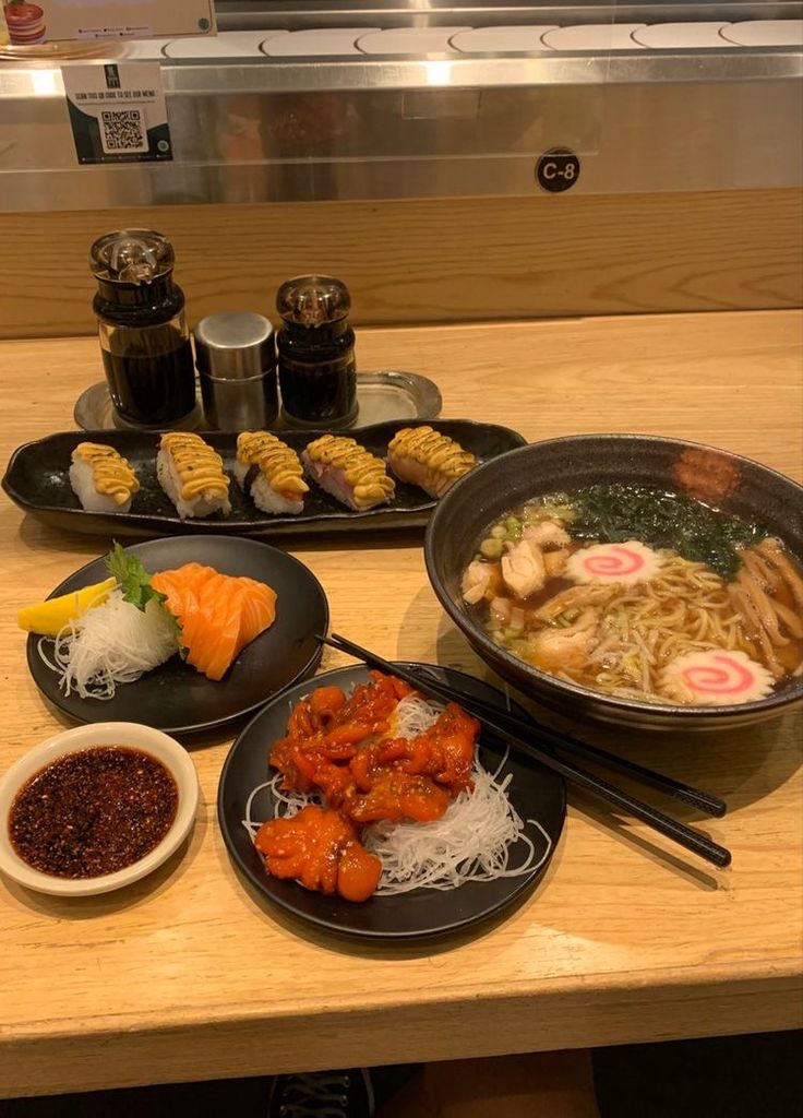 a table topped with plates of food and chopsticks next to bowls of sauce