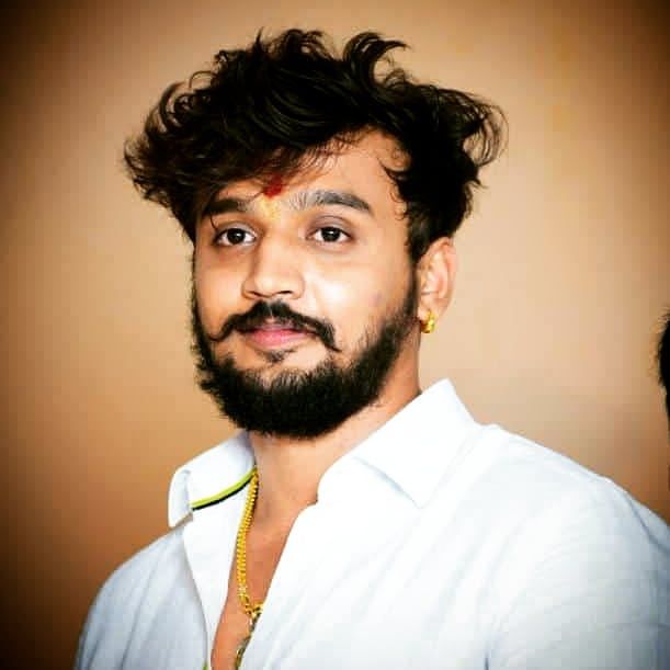 a man with a beard wearing a white shirt and gold necklace on his neck is looking at the camera