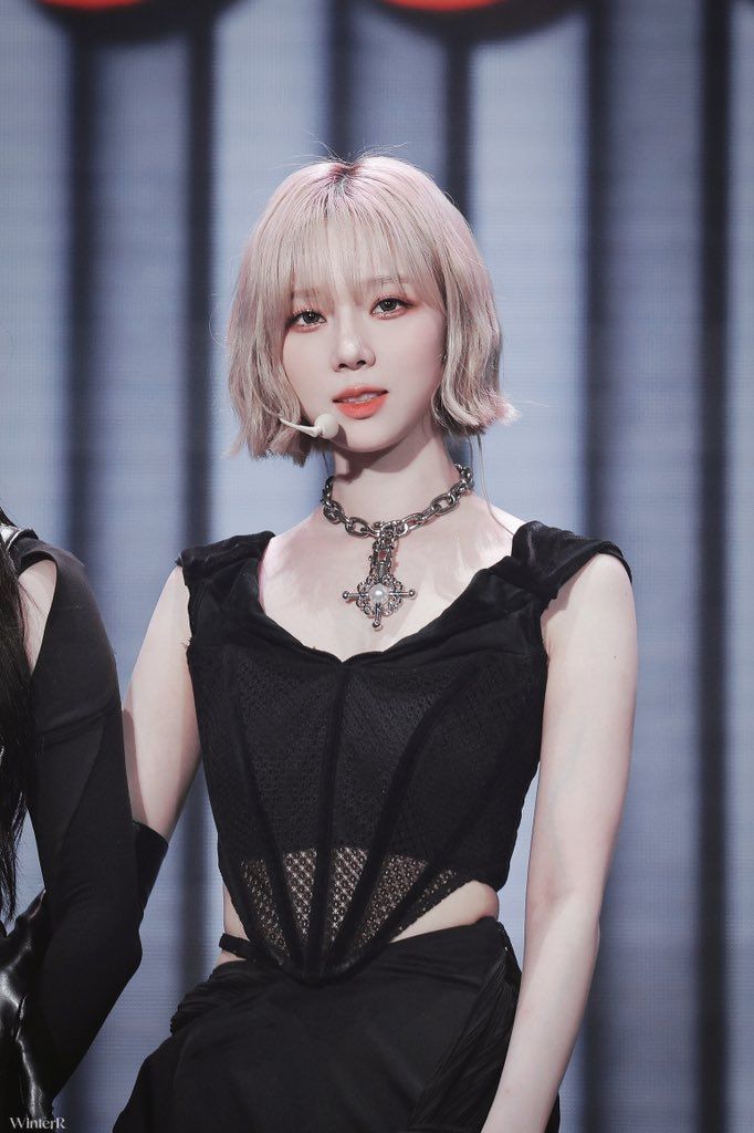 a woman with short blonde hair wearing a black dress and choker on the runway