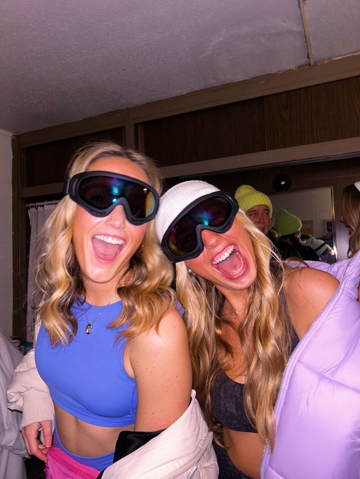 two beautiful women standing next to each other in front of a mirror with goggles on