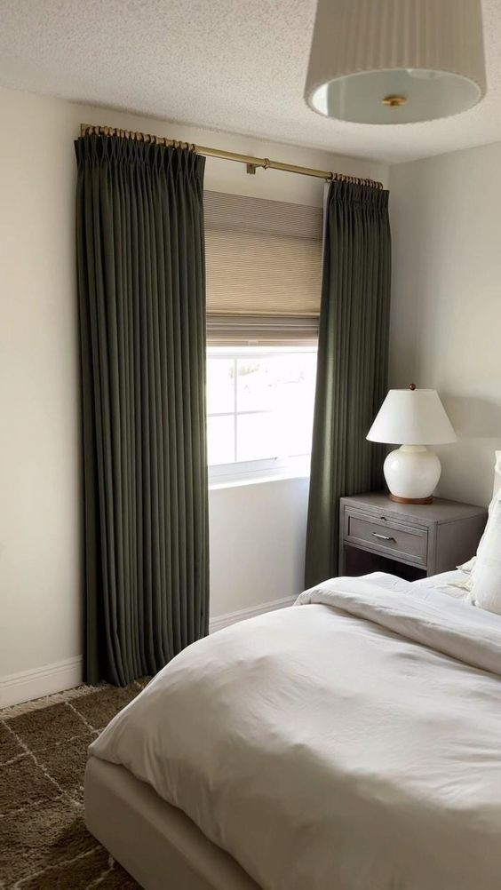 a white bed sitting next to a window in a room with green curtains on the windowsill