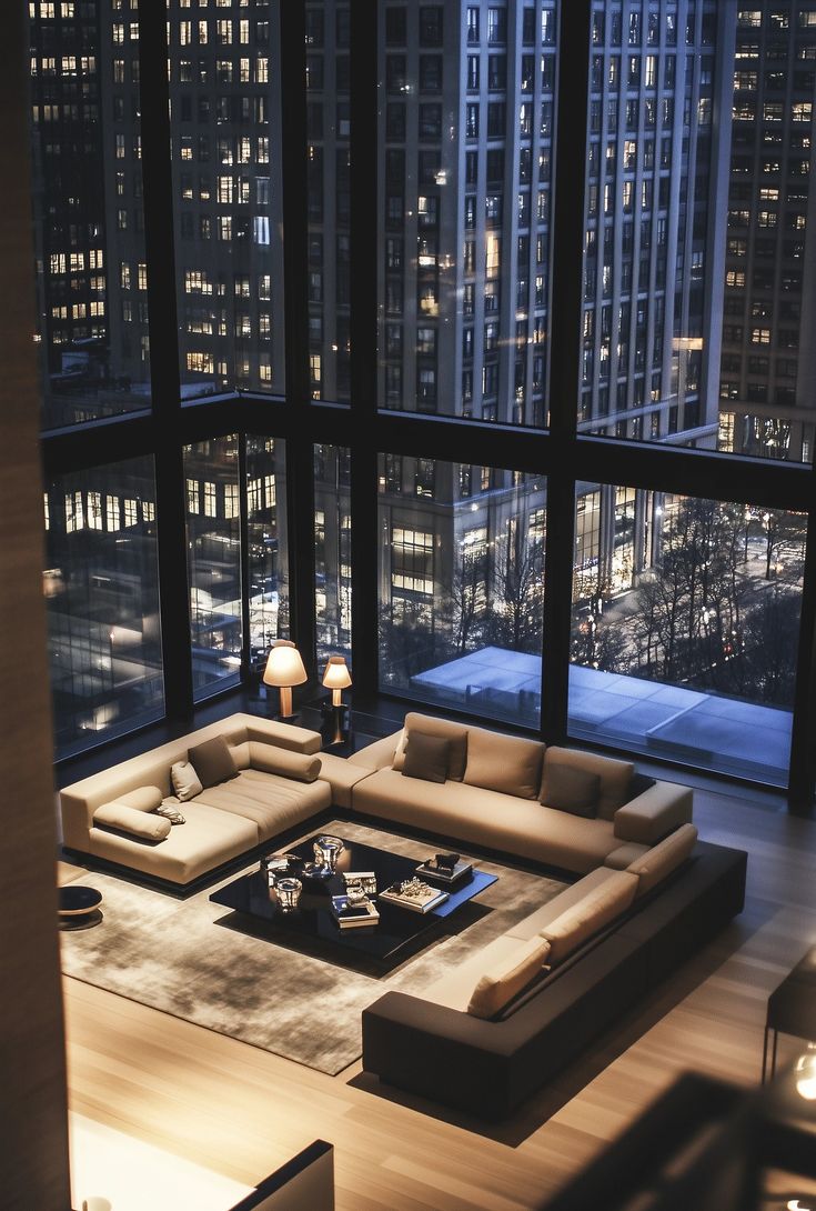 a living room filled with lots of furniture and tall buildings in the background at night