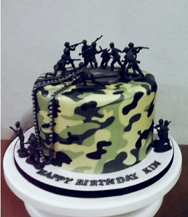 a birthday cake decorated with camo and soldiers on it's side, sitting on top of a white pedestal