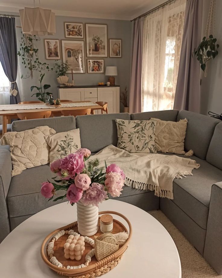 a living room filled with furniture and flowers on top of a white table in front of a window