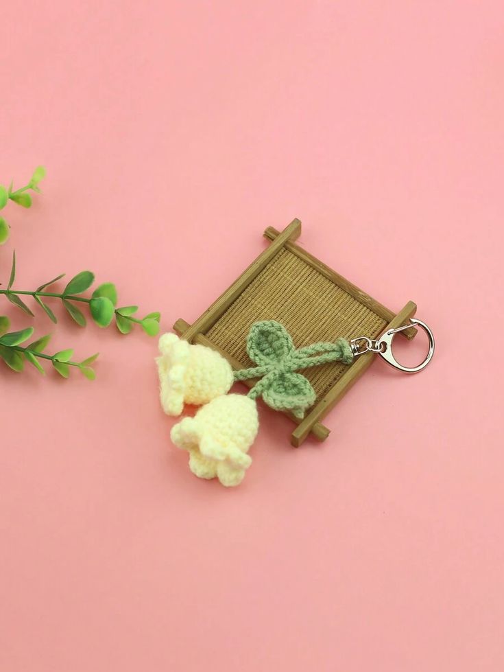 two crocheted sheep keychains sitting on top of a pink surface next to a plant