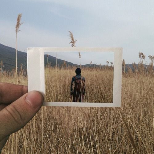 a person standing in a field holding up a polaroid with the image of a man