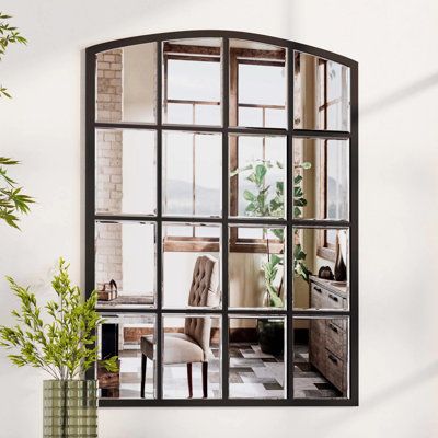 a mirror reflecting a living room with chairs and plants in the window sill, next to a potted plant