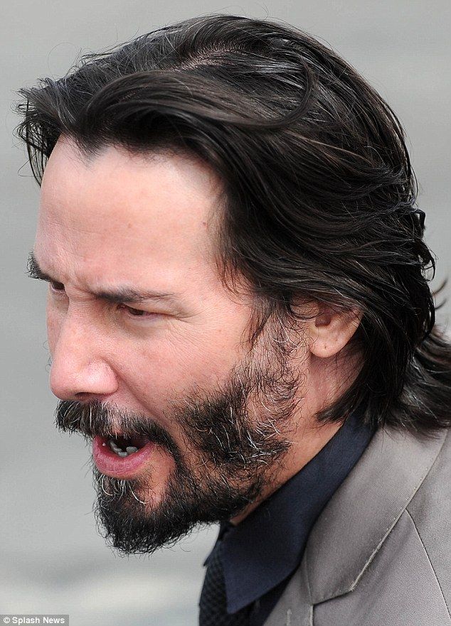 a man with long black hair and beard wearing a suit looks off to the side