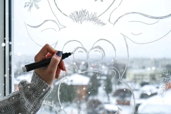 a person drawing on a frosted window with a marker and pen in their hand