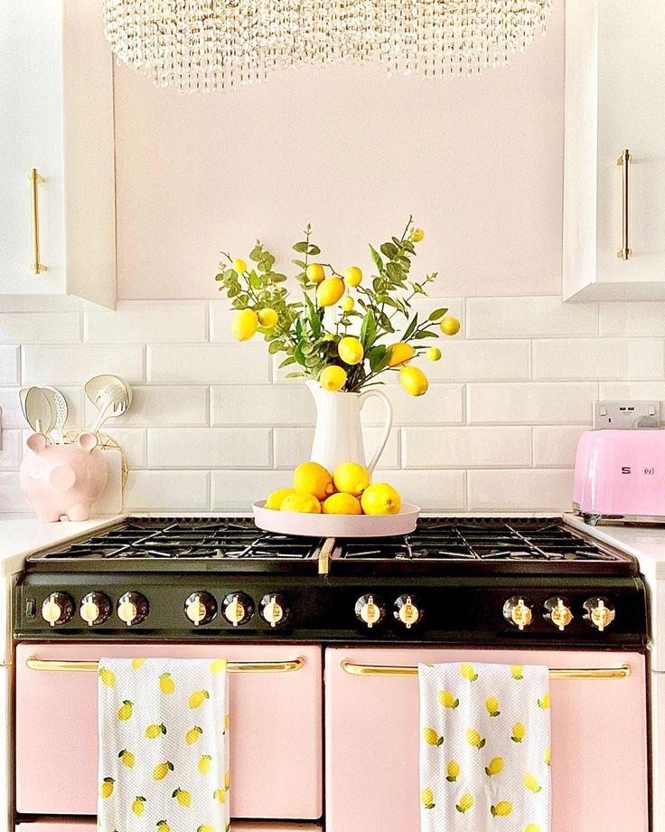 a pink and white kitchen with lemons in a vase on the gas stove top