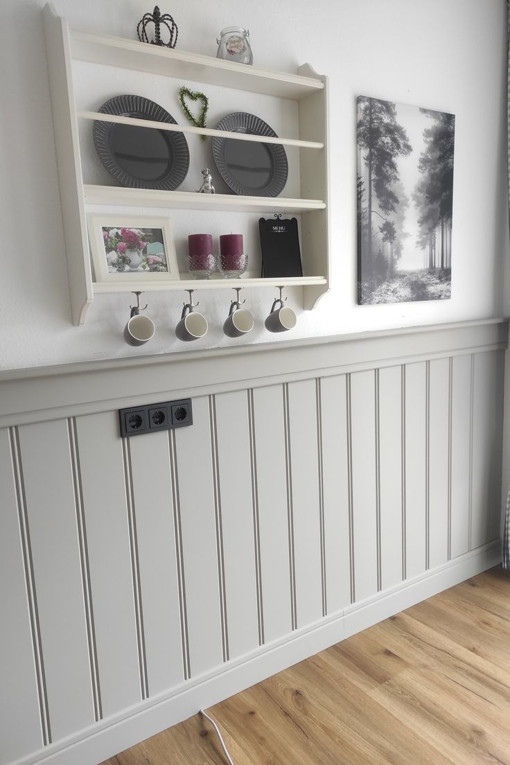 a kitchen with white walls and wooden floors, plates on the shelf above the stove