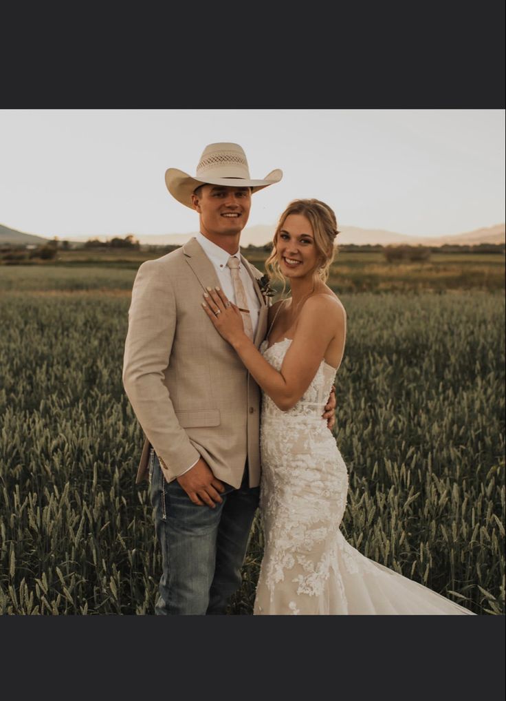 a bride and groom standing in the middle of a field wearing cowboy hats for their wedding