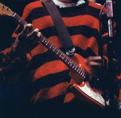 a man with long hair holding a guitar in front of a microphone and wearing a striped shirt