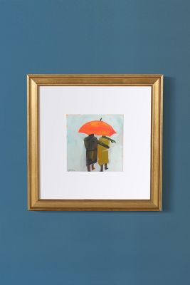 two people standing under an orange umbrella in front of a blue wall with a gold frame