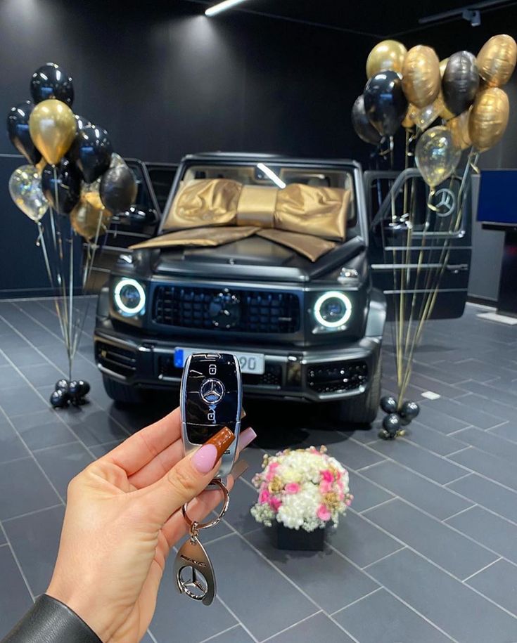 a person holding up a cell phone in front of a car with balloons and flowers