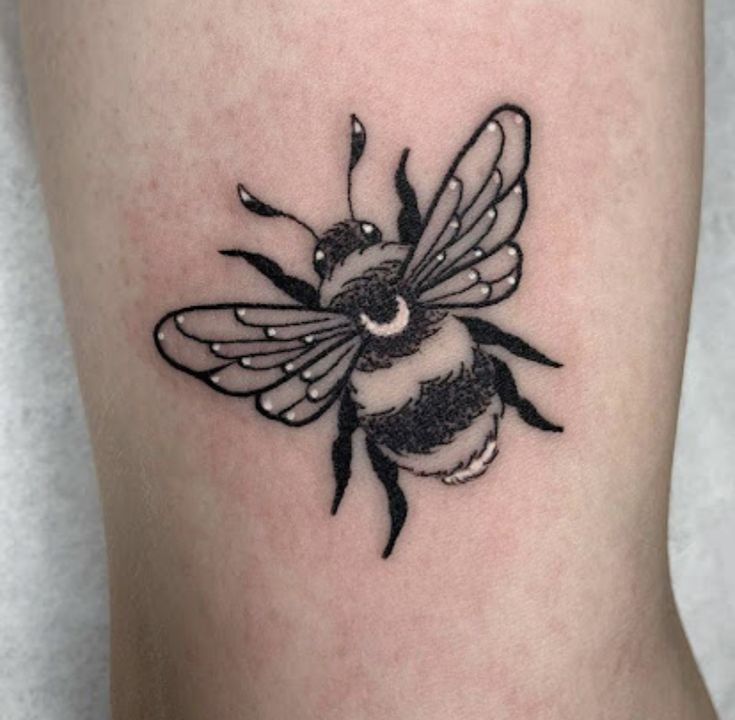 a small black and white tattoo of a bee on the right side of the leg