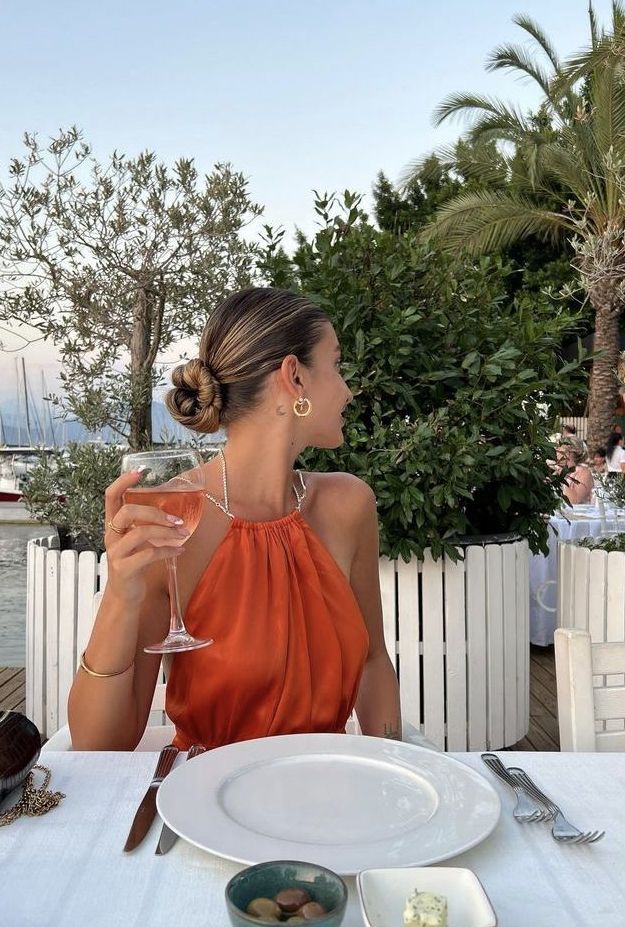 a woman sitting at a table with a glass of wine in her hand and plates on the table