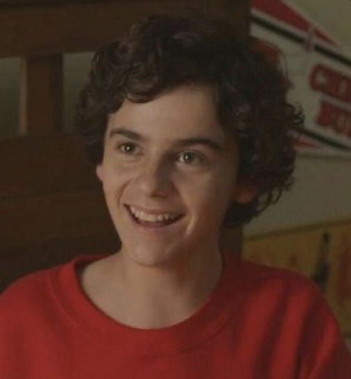 a young boy is smiling and holding a lit candle in his hand while sitting on the bed