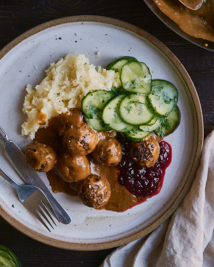 a white plate topped with meatballs, mashed potatoes and cucumbers