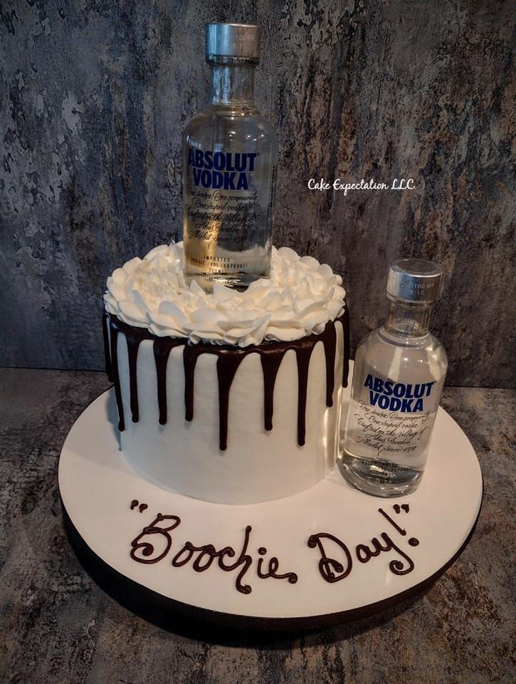 a birthday cake with vodka bottle on top and chocolate drizzled around it