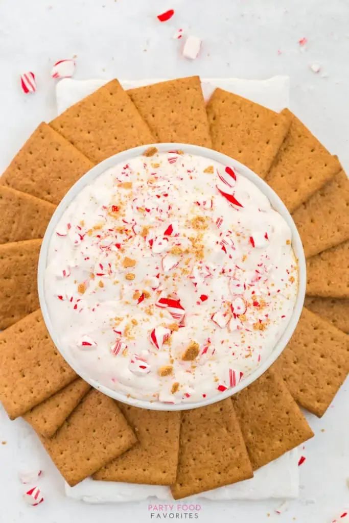 a white bowl filled with whipped cream surrounded by crackers and candy canes on top