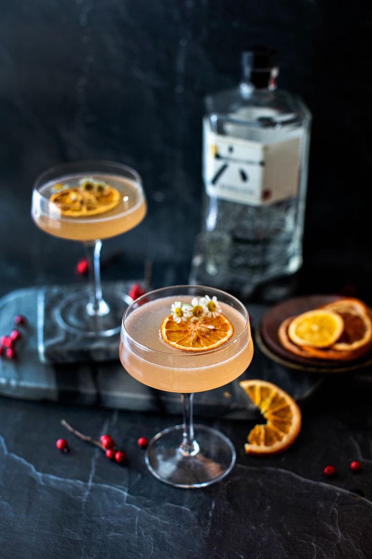 two glasses filled with orange slices and garnished with cranberries on a black surface