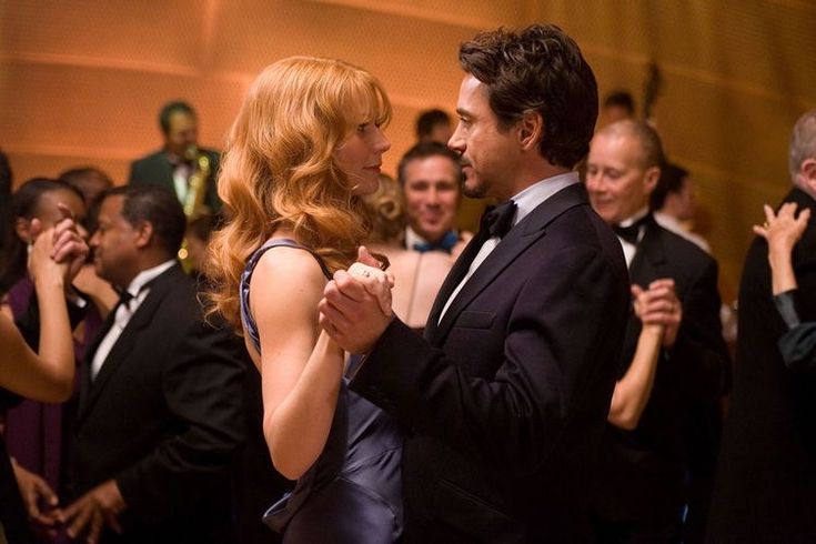 a man and woman dance together in front of a large group of people wearing tuxedos