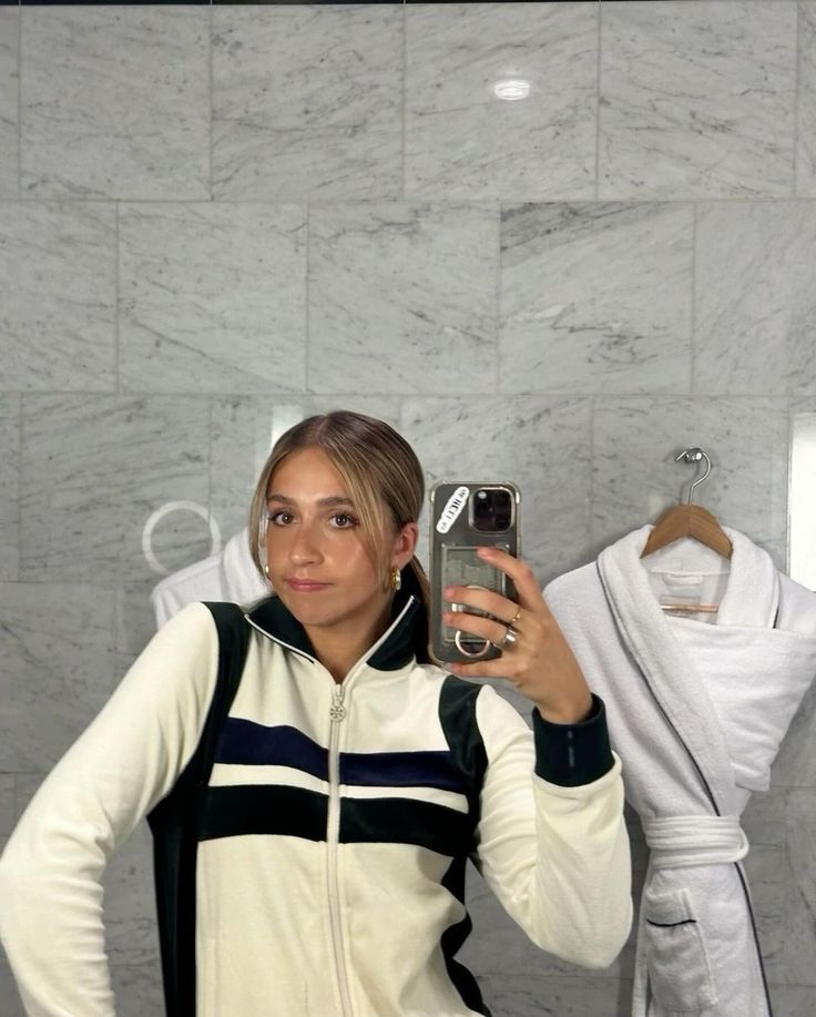 a woman taking a selfie with her cell phone in front of a bathroom mirror