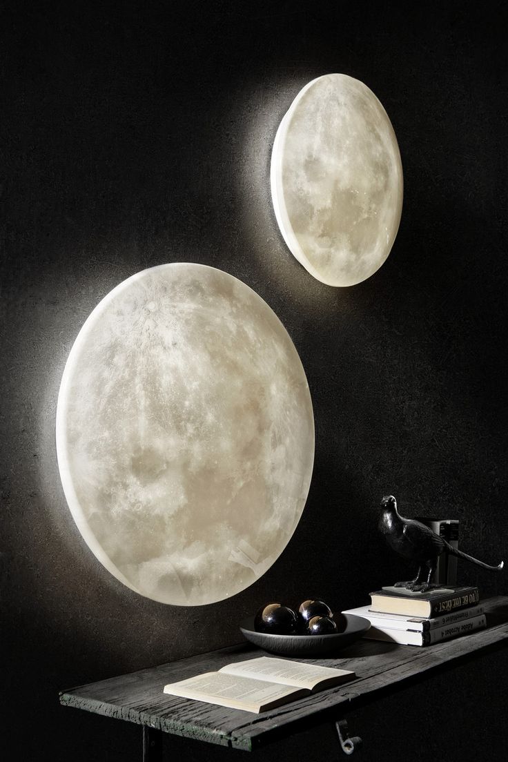 two moon lights are on the wall above a table with books and an alarm clock