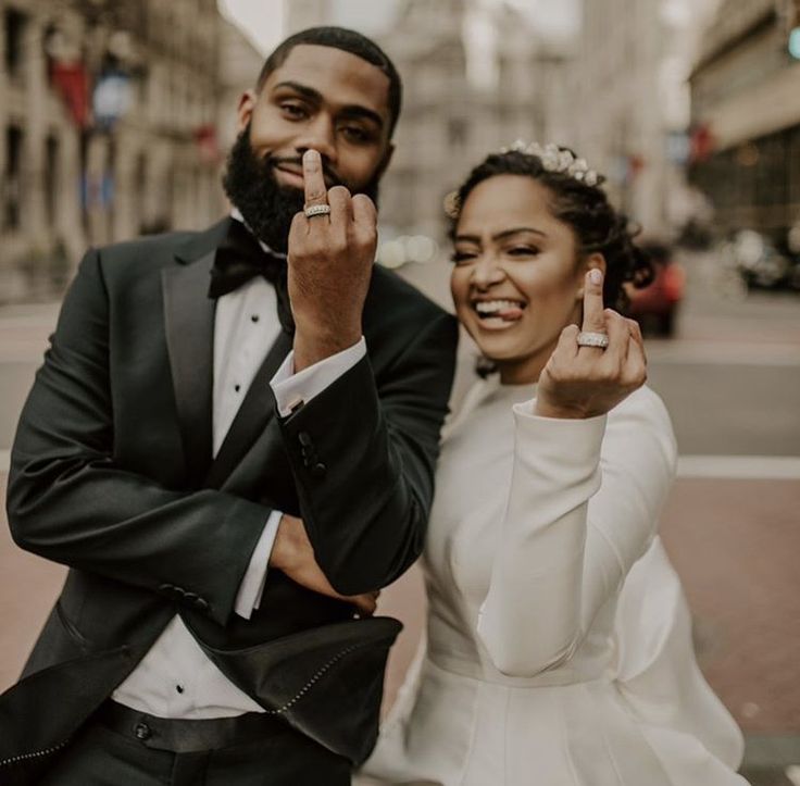 a bride and groom pose for a photo on the street with their fingers in the air