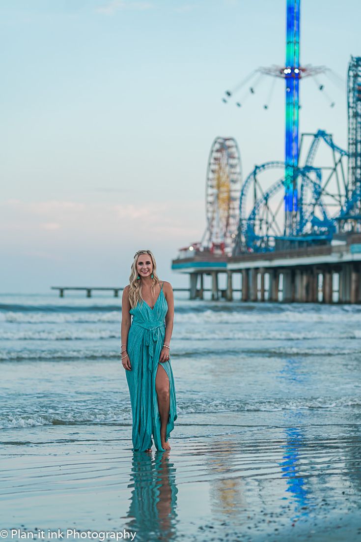 a woman in a blue dress standing on the beach with roller coasters in the background