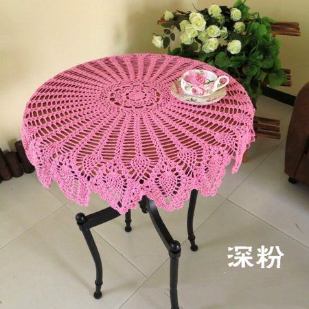 a pink crocheted table with a cup on it and flowers in the background