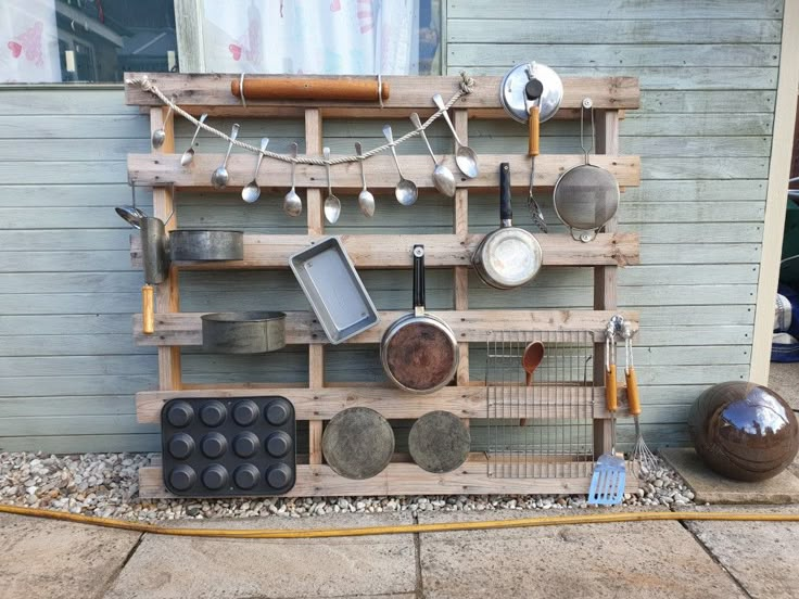 a wooden rack with pots and pans hanging from it's sides on the side of a house