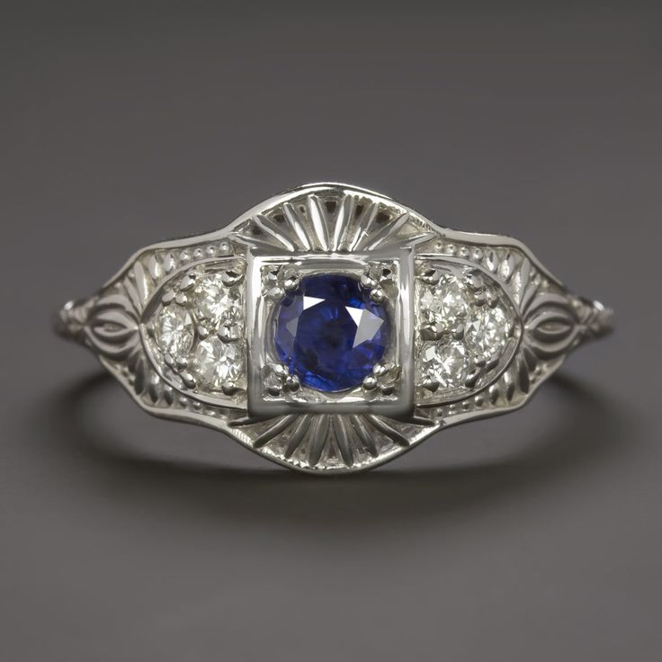 This beautiful and unique ring features a richl blue sapphire set in a diamond studded vintage style design that will never go out of style! The sapphire has a richly saturated blue hue that contrasts strikingly with the 14k white gold setting. Utterly classic and romantic, the antique style setting is richly textured Classic Sapphire Halo Ring, Classic Sapphire Birthstone Ring, Art Deco Blue Diamond Ring With Accents, Art Deco Blue Diamond Ring With Center Stone, Art Deco Blue Sapphire Ring With Center Stone, Blue Art Deco Diamond Ring With Center Stone, Classic Royal Blue Round Sapphire Ring, Blue Art Deco Diamond Ring With Accents, Classic Blue Sapphire Ring In 14k White Gold