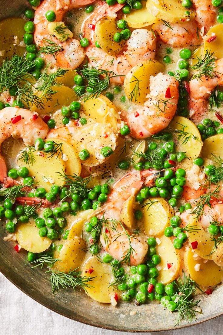 a pan filled with shrimp, potatoes and peas on top of a white table cloth