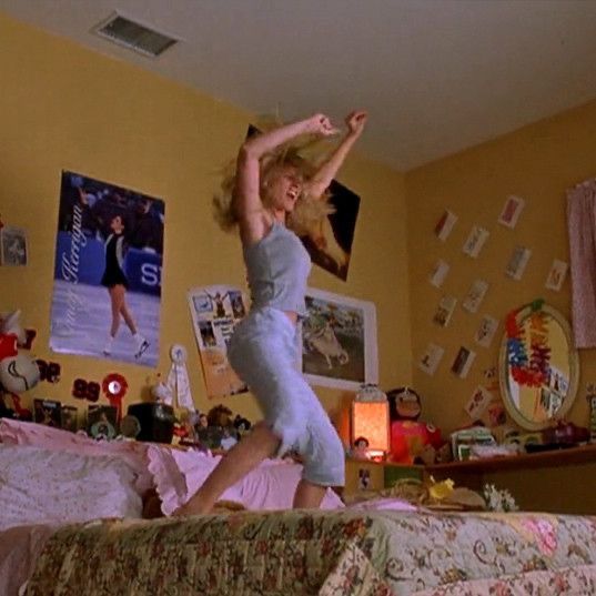 a woman jumping on top of a bed in a room filled with pictures and furniture