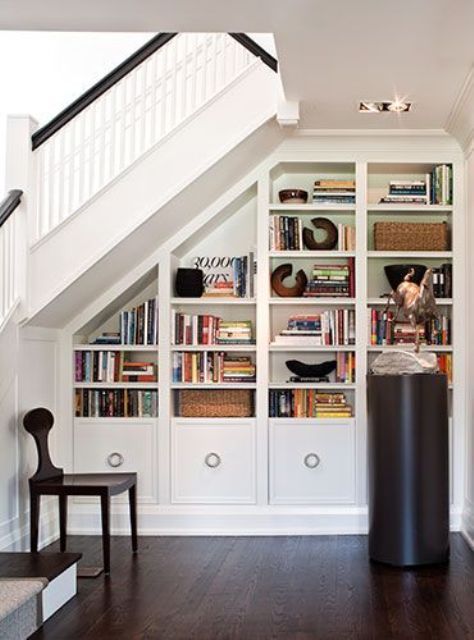 the bookshelves in this home are full of books and magazines, while the stairs lead up to the second floor