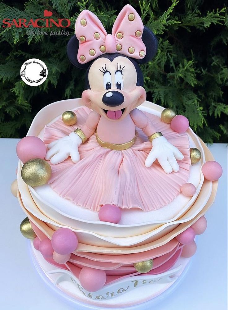 there is a cake made to look like minnie mouse on top of stacked plates with gold and pink decorations