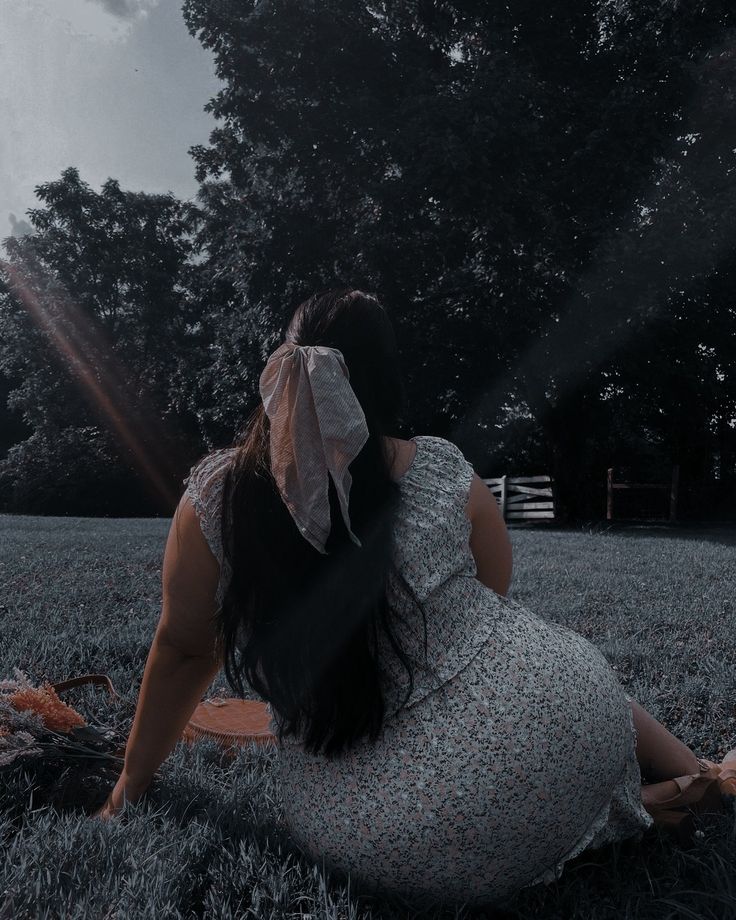 a woman sitting in the grass with her back to the camera