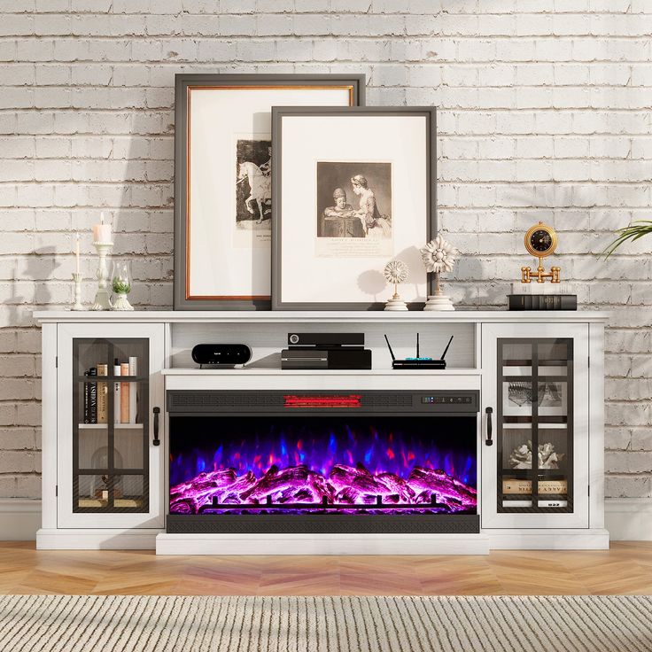 a white entertainment center with an electric fireplace in front of a brick wall and framed pictures