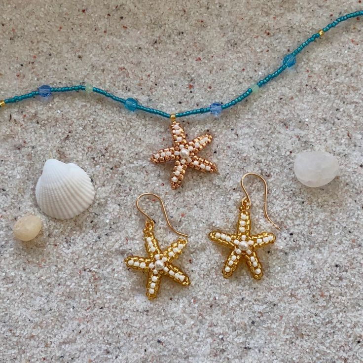 three starfish earrings are laying on the ground next to shells and beads, along with a blue beaded necklace