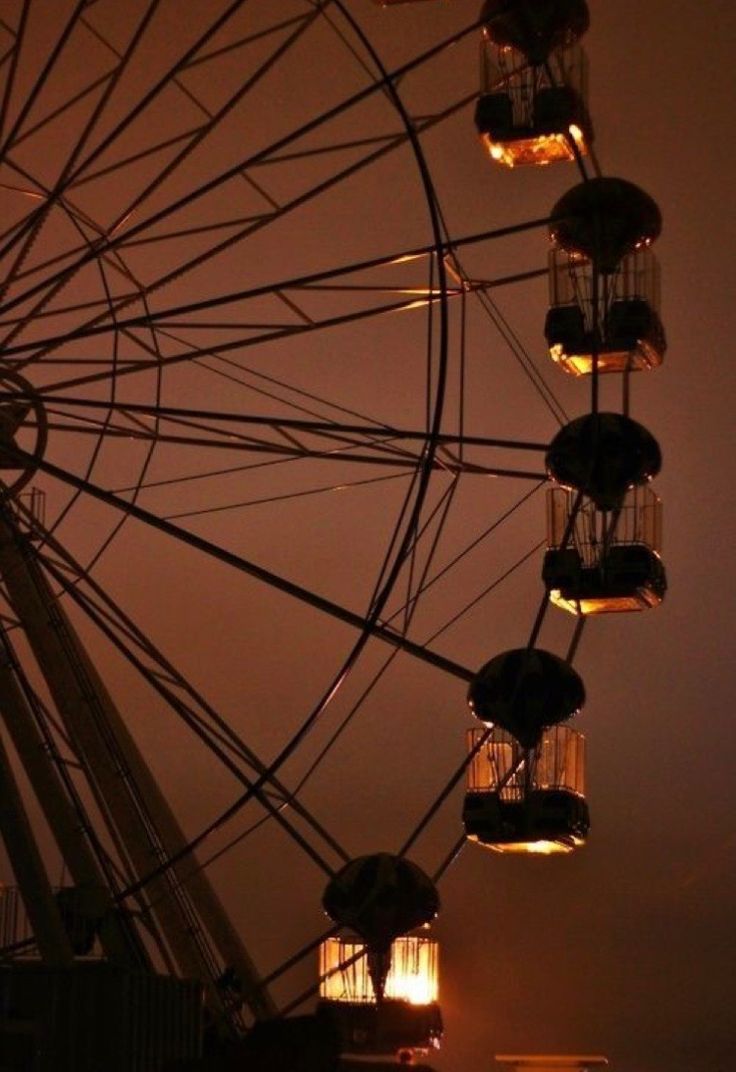 a ferris wheel lit up at night with its lights turned on and the sky in the background