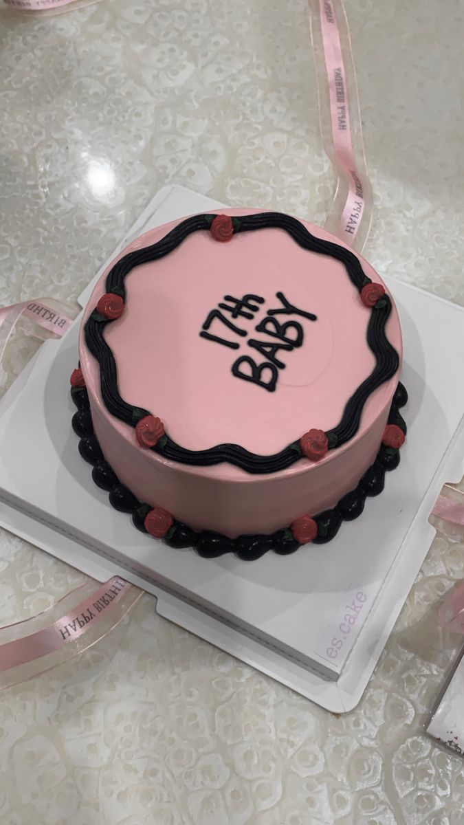 a pink and black cake with the words baby on it sitting on a white plate