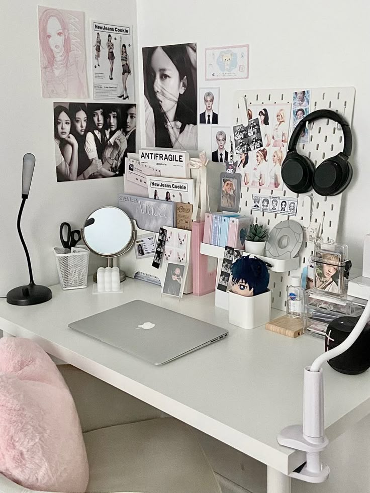 a white desk topped with a laptop computer next to a pink pillow and headphones