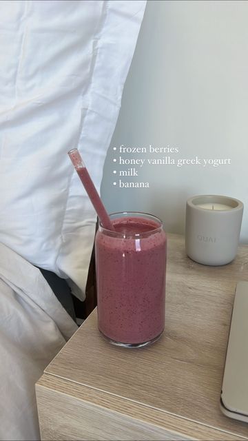 a pink smoothie in a glass next to a laptop on a wooden table with a white pillow