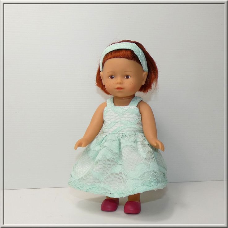 a doll with red hair wearing a blue dress and pink shoes is standing on a white surface