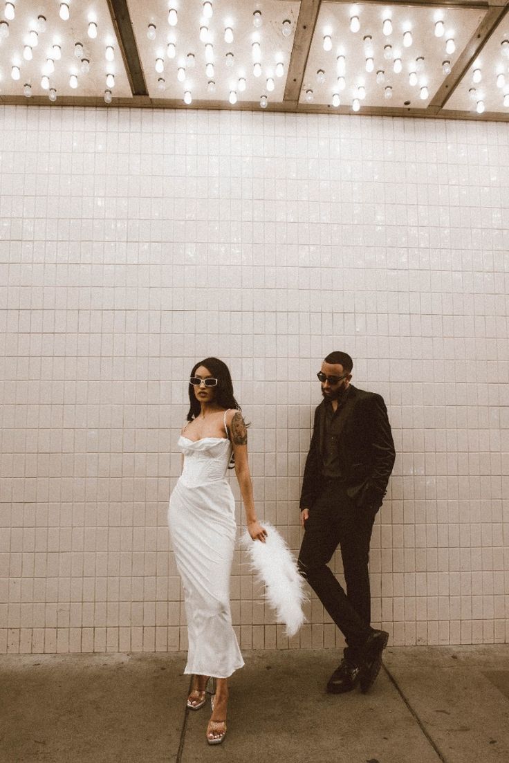 a man and woman standing next to each other in front of a white tiled wall